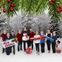 Group of people holdng various christmas decorations in front of a snowy woodland background 