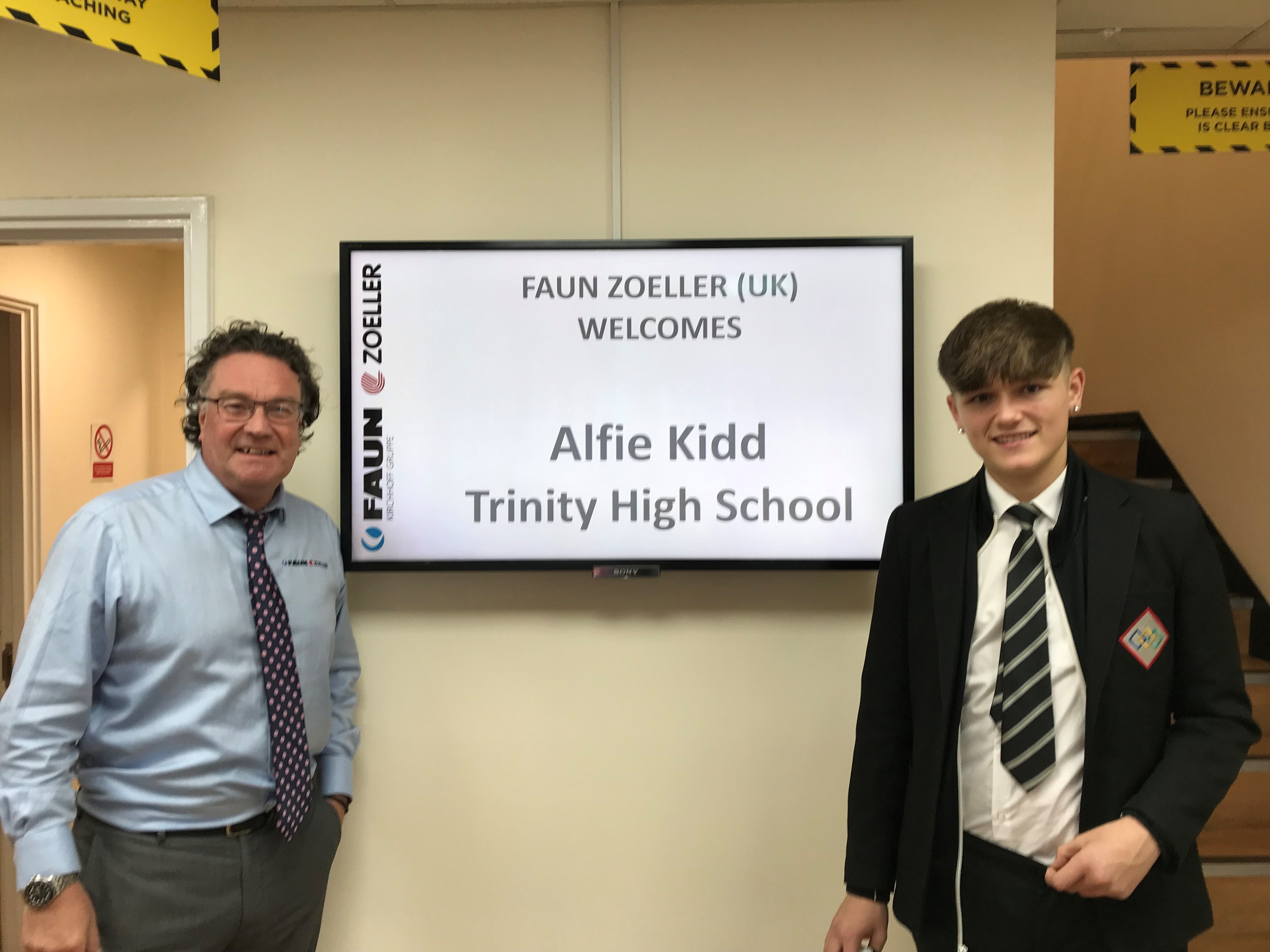 Image shows Alfie Kidd and Simon Hyde standing either side of a TV screen which shows a welcome message for Alfie