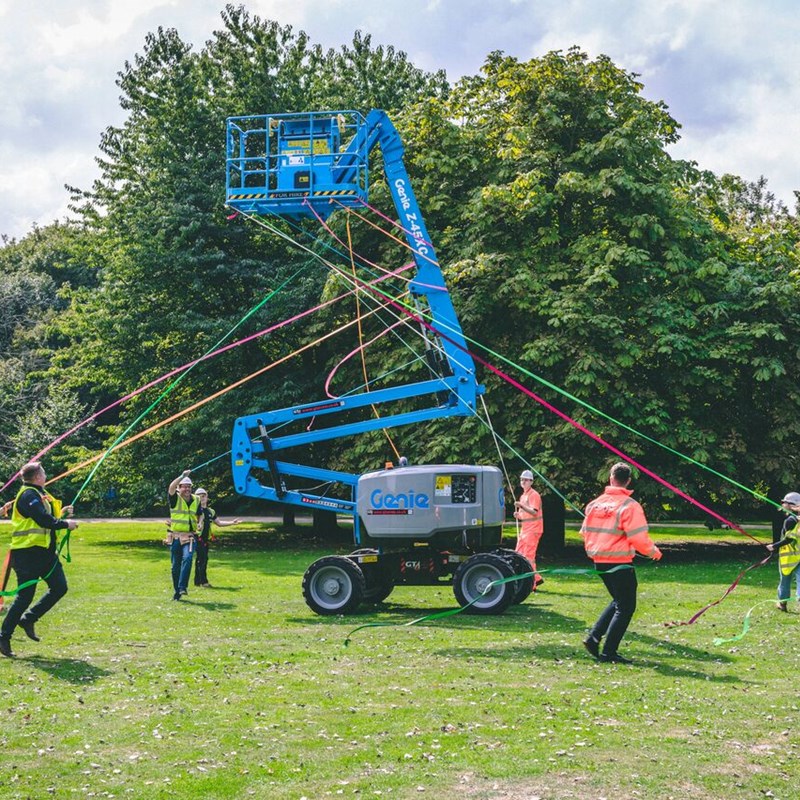 Group of people maypole dancing around a cherry picker