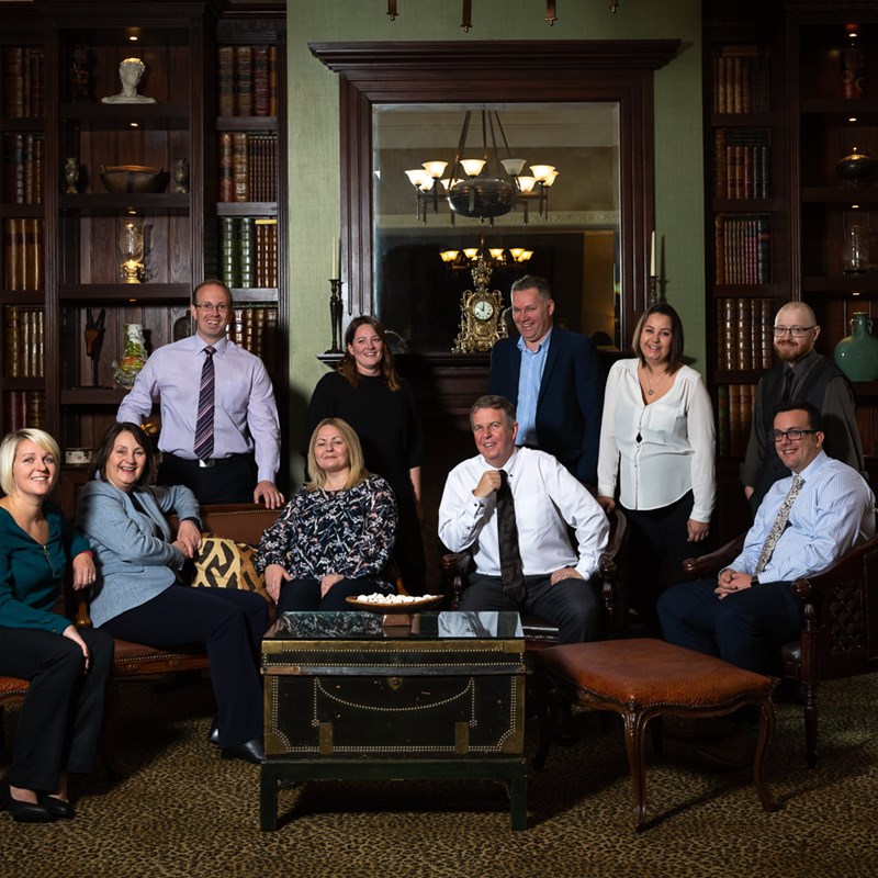 Group of 10 people stood and sat in formal drawing room style room all smiling at camera