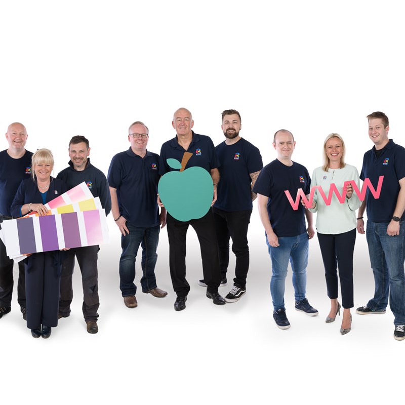 12 people in groups of 3, each group holding prop, 1 group has colour swatches, 1 an apple cutout, 1 the letters www and 1 a pen.