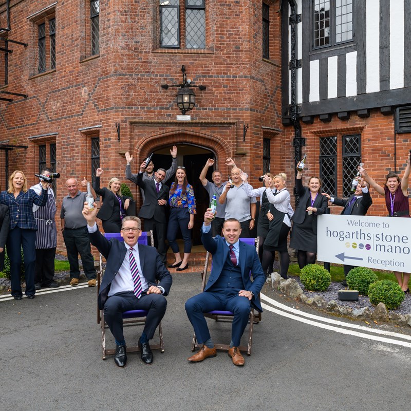 several people outside the hotel with bottles of wine holding in the air
