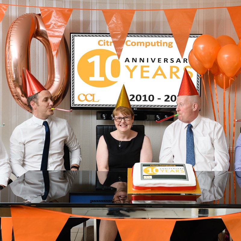 5 people sat in front of logo celebrating 10 years with ballons and whistles