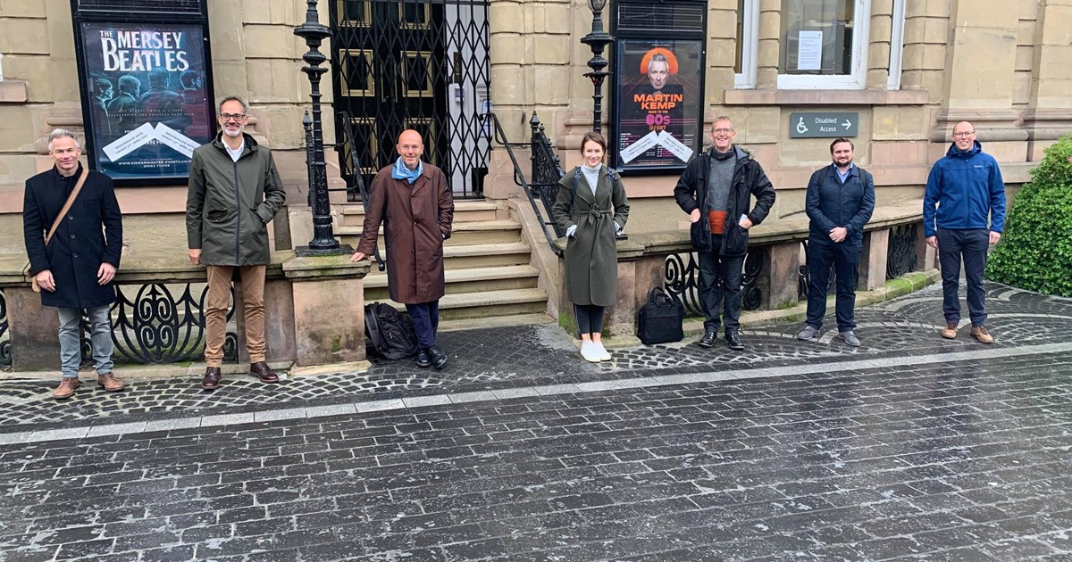 group of people social distancing stood outside town hall building in town centre