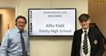 Image shows Alfie Kidd and Simon Hyde standing either side of a TV screen which shows a welcome message for Alfie