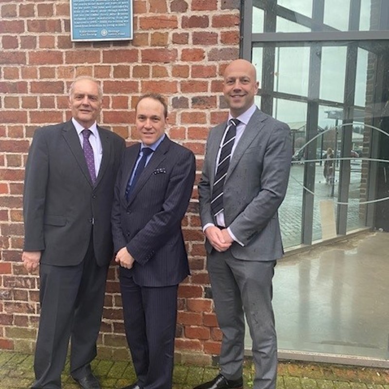 3 men in suits in front of red brick with plaque reading piano building